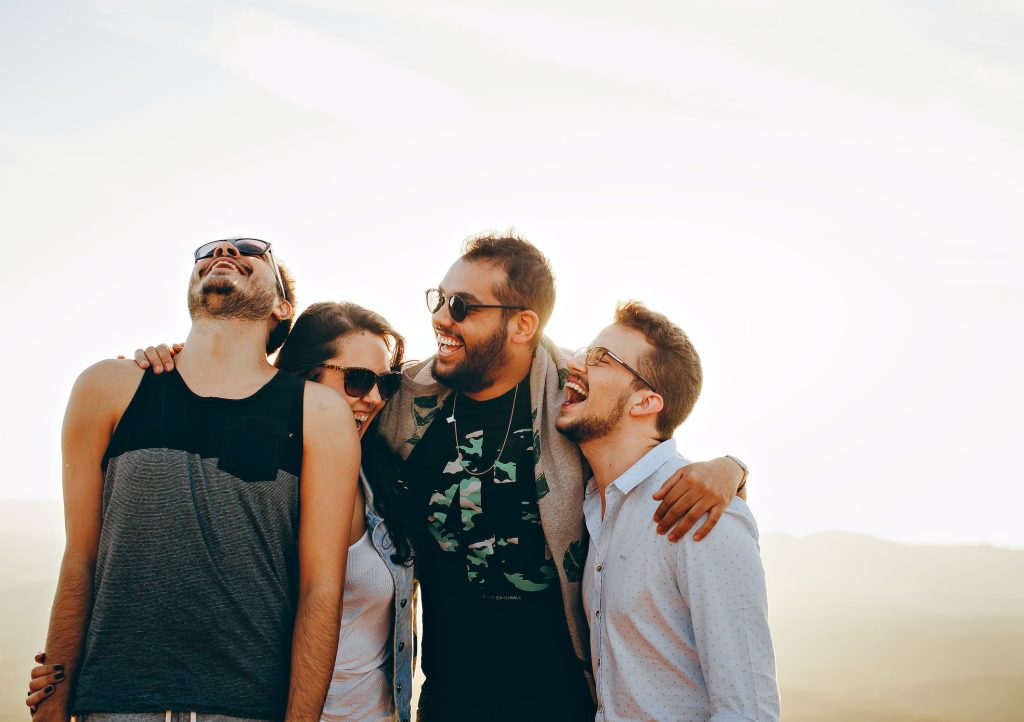 A group of friends smiling and wearing sun glases in front of a picturesque nature backdrop.