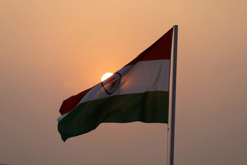 Indian flag waving in the air with the sun behind it at dusk