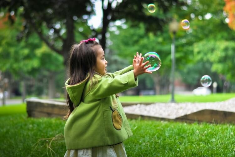 a young asian girl chases a bubble outside on the grass