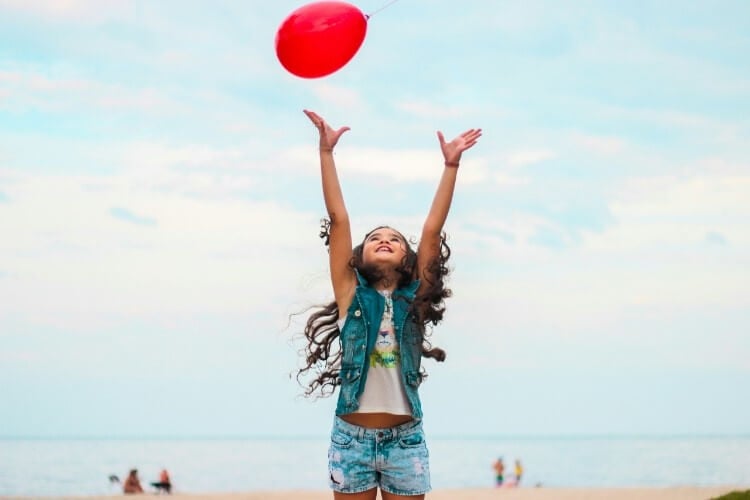 a young girl jumps to catch a balloon on the beach