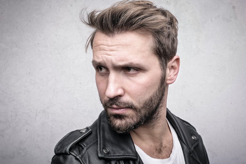 Rugged looking man in a leather jacket posing for a photo while looking to the left