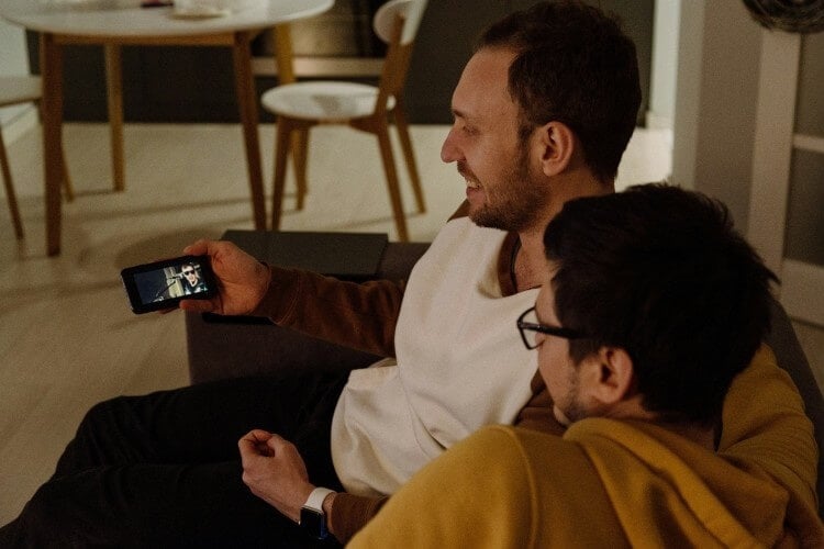 Couple sits on couch and watches videos on one man's phone