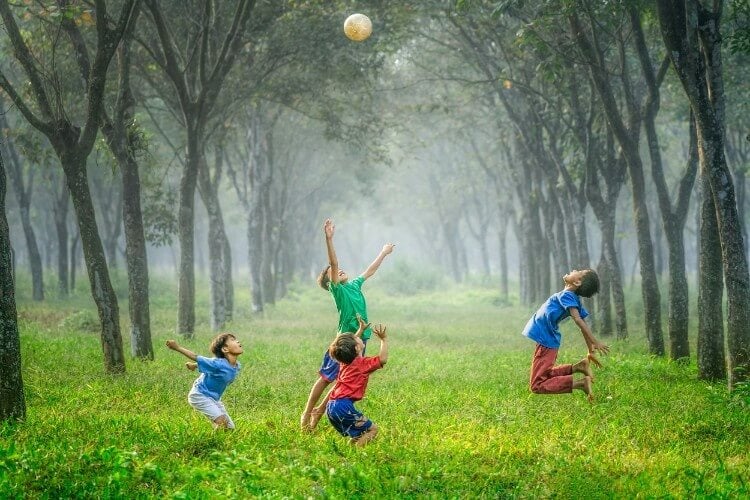 four kids play in a forest outside and throw a ball in the air. they are happy and jumping