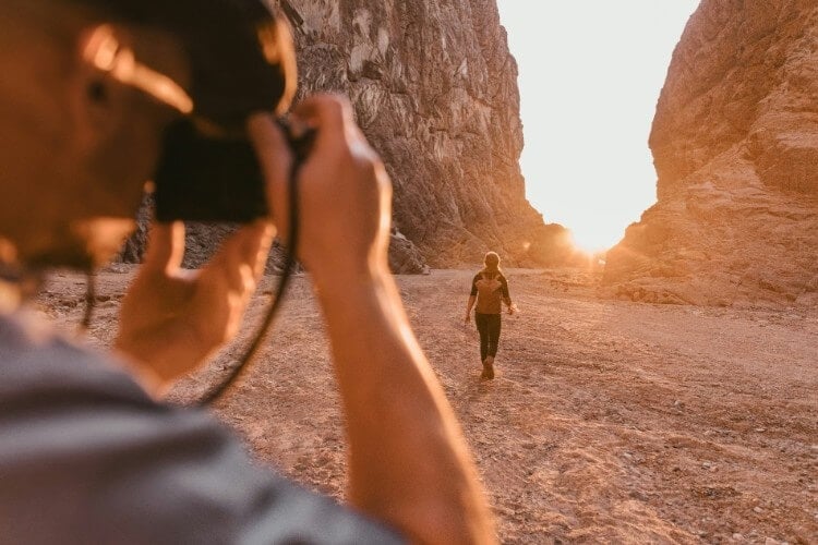 Man films woman walking in desert canyon